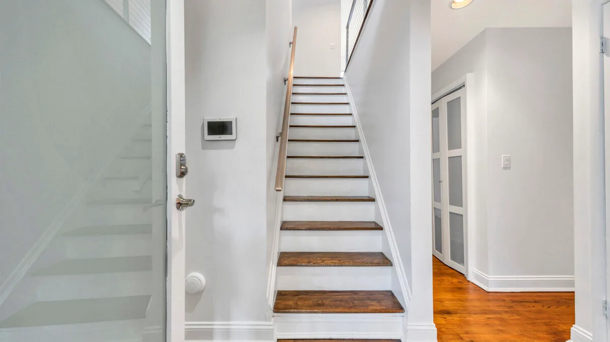A bright interior hallway with a staircase and wooden flooring.