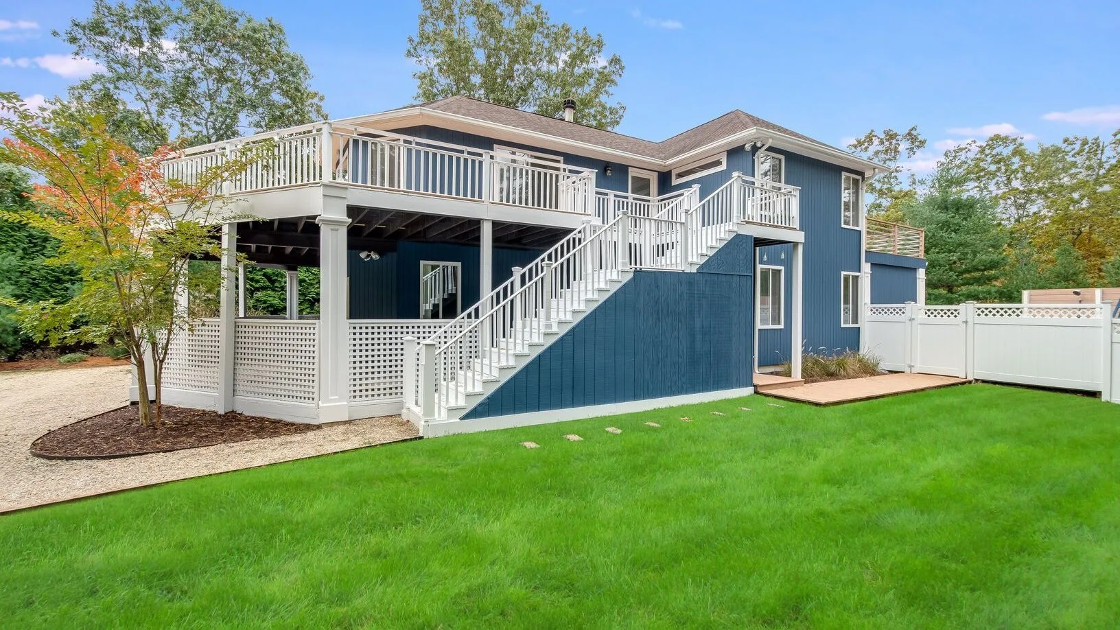 A raised blue house with white railings overlooks a green lawn.