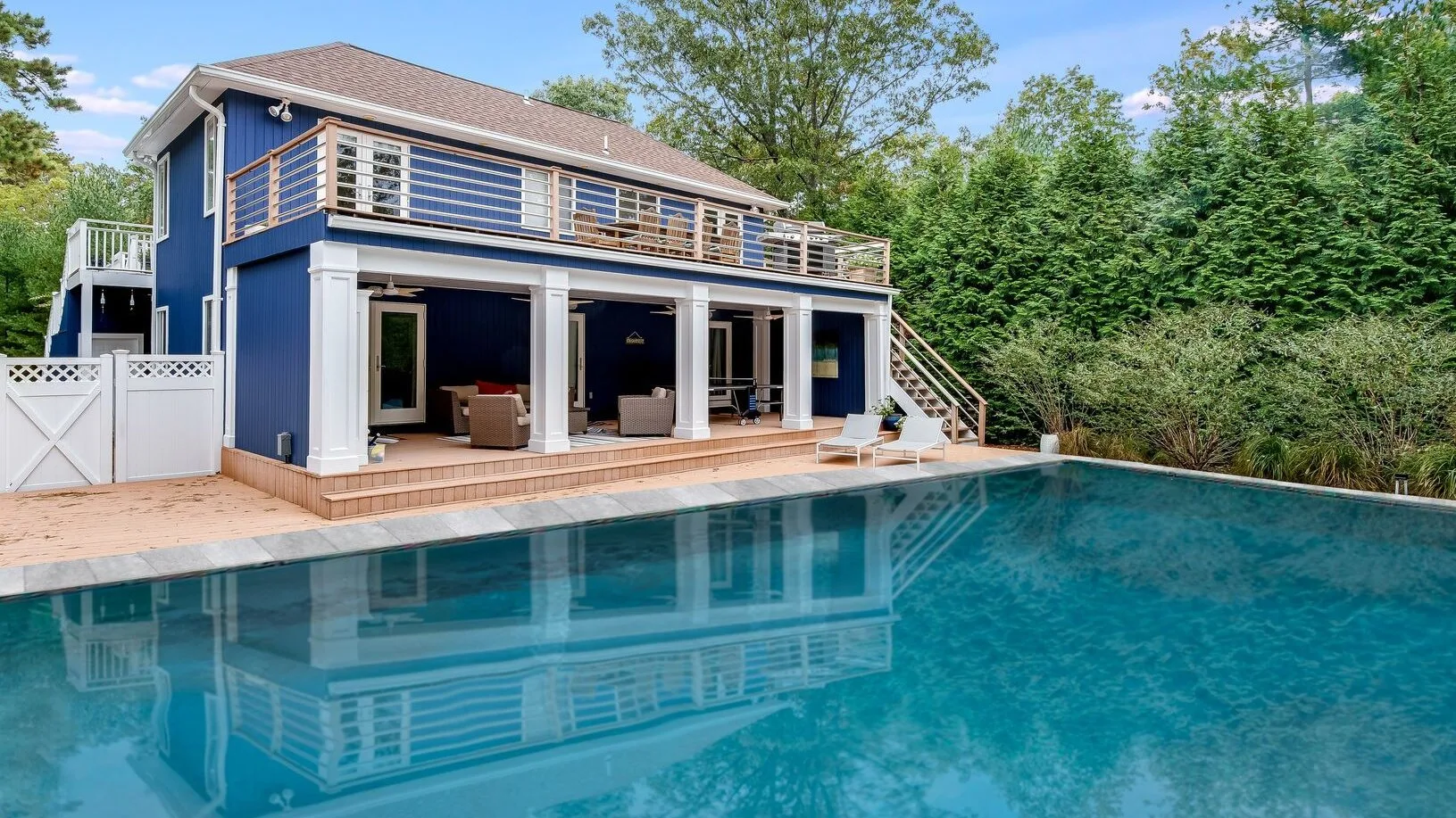 A blue house overlooks a swimming pool, with a covered patio and upper deck.