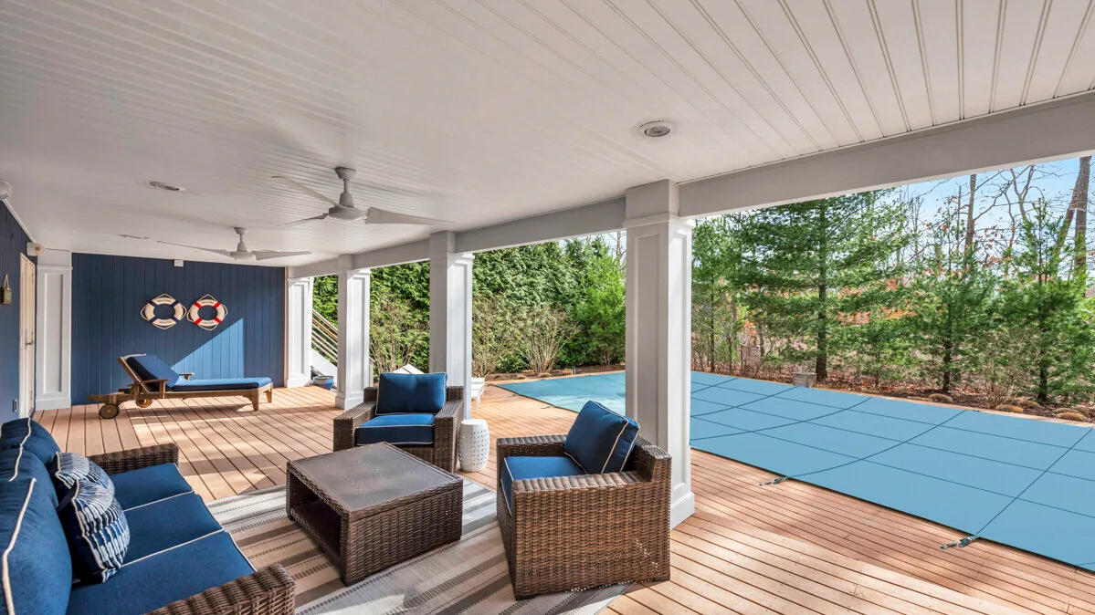 A covered outdoor seating area overlooks a blue swimming pool and surrounding trees.