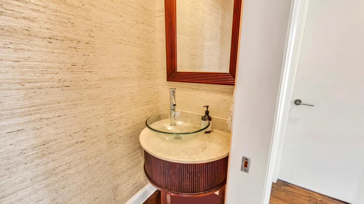 A bathroom vanity with a round glass sink sits beneath a framed mirror.