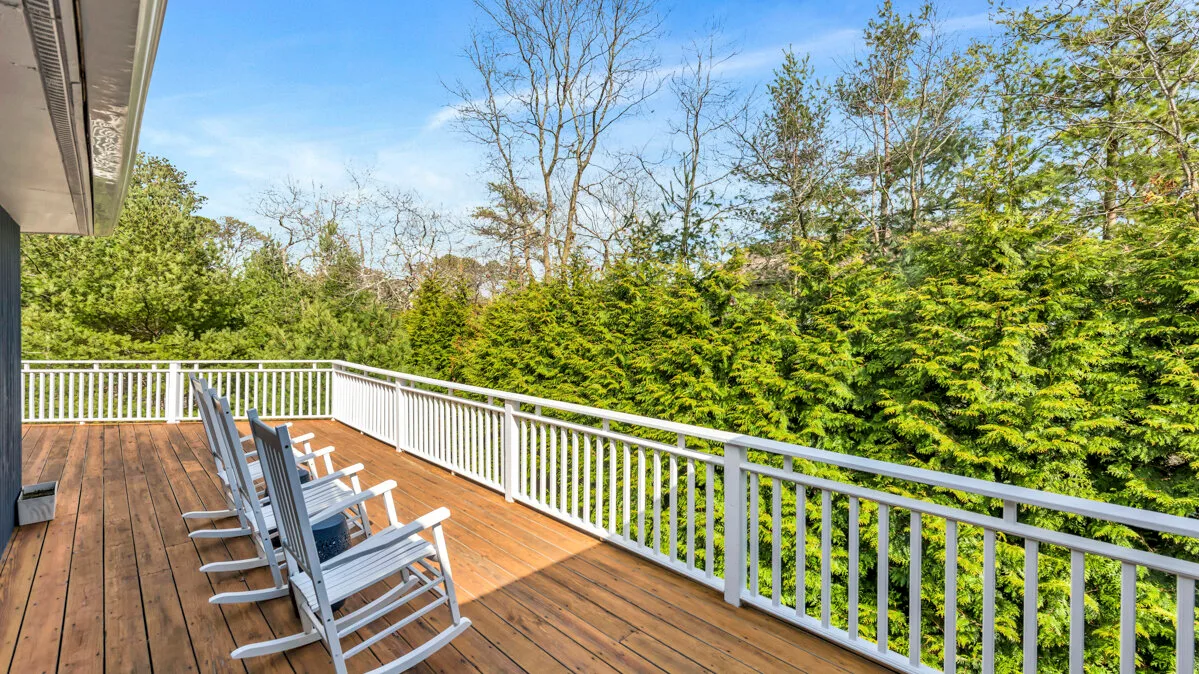 A wooden deck with seating overlooks dense green trees.