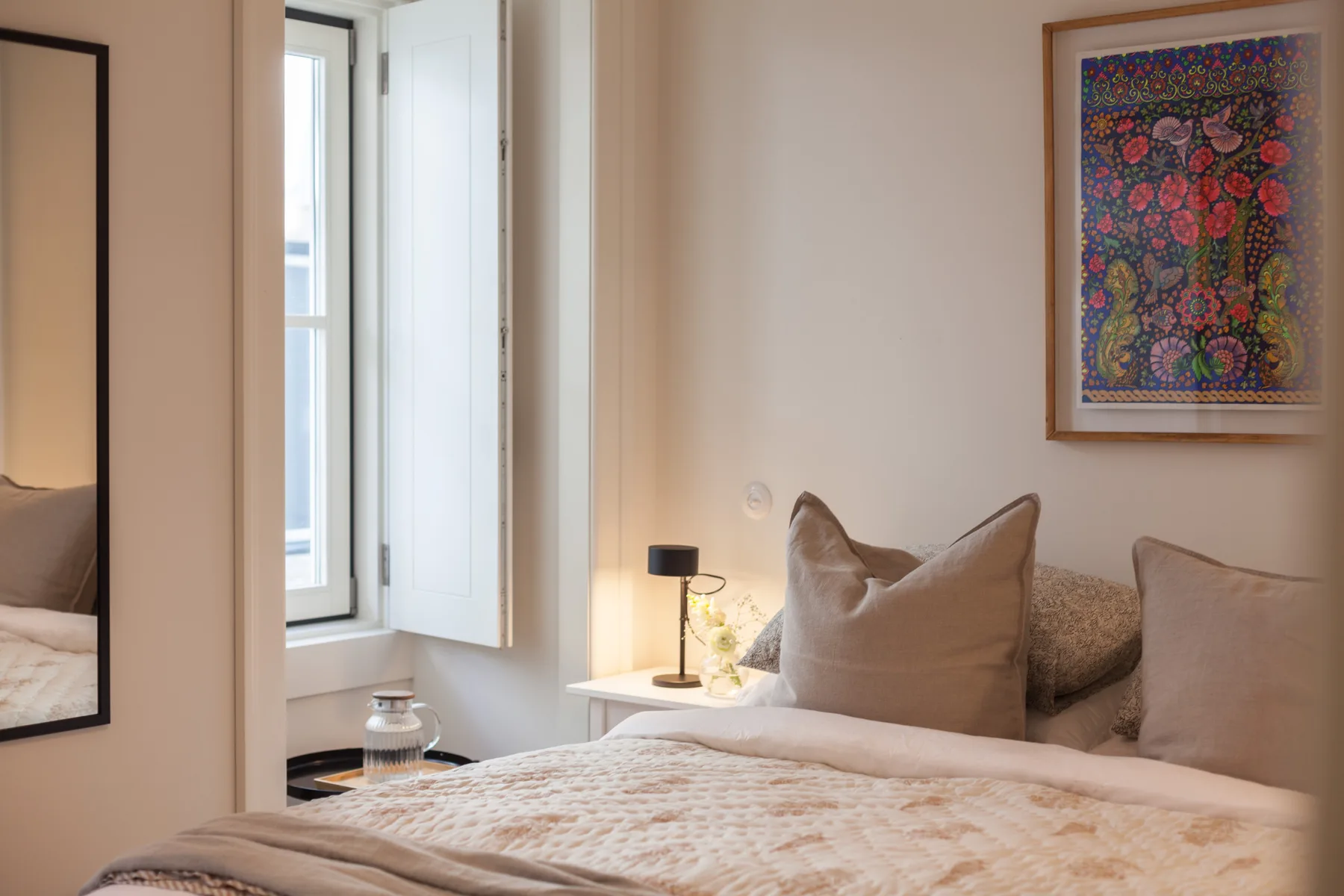 A bedroom with a bed, bedside lamp, and colorful framed artwork.