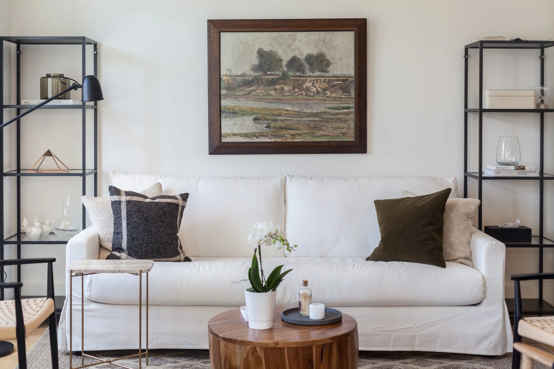 A living room with a white sofa, coffee table, and framed landscape painting.