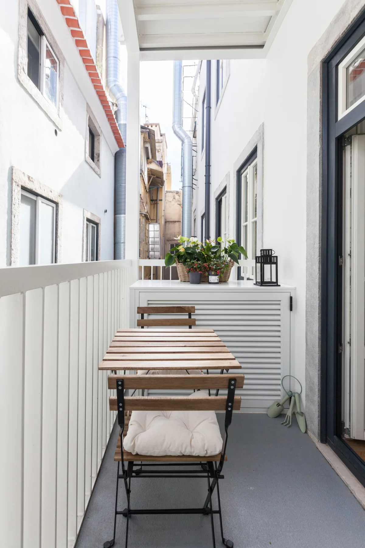 A narrow outdoor patio with a wooden table, seating, and potted plants.