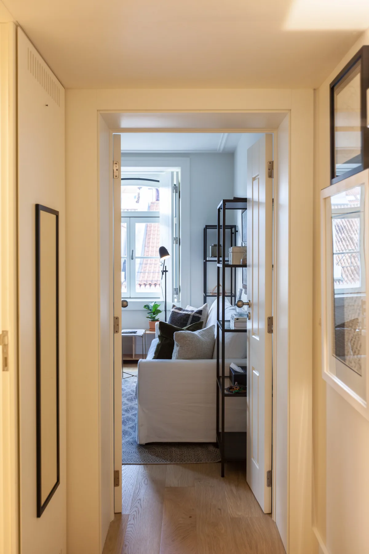 A hallway opens into a bright living area with seating and large windows.