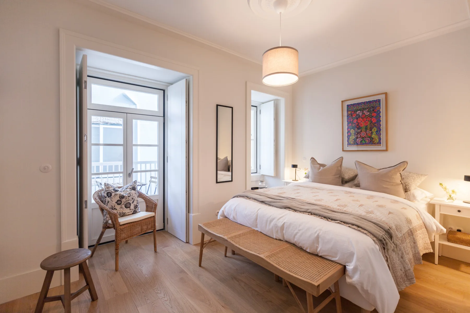 A bright bedroom with a bed, bench, and an open doorway to a balcony.