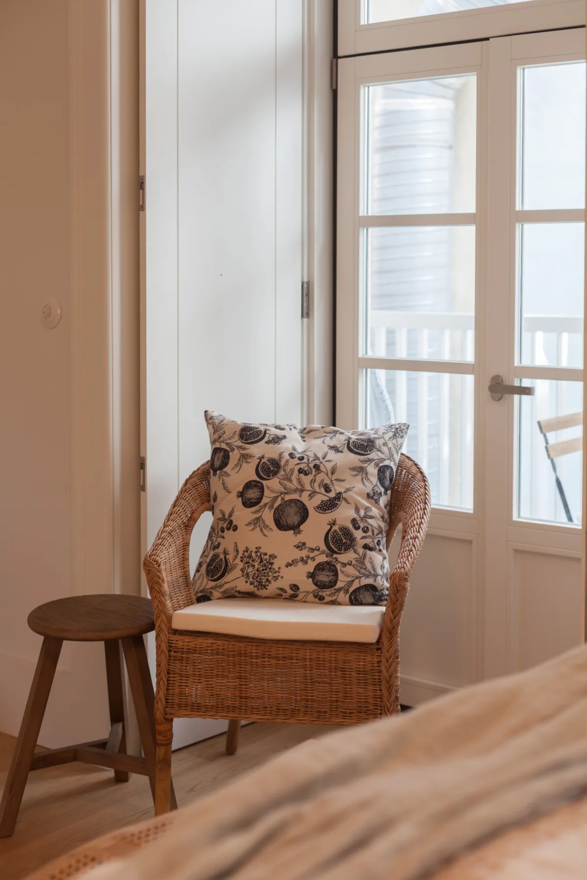 A wicker chair with a patterned cushion sits beside a bright glass door.