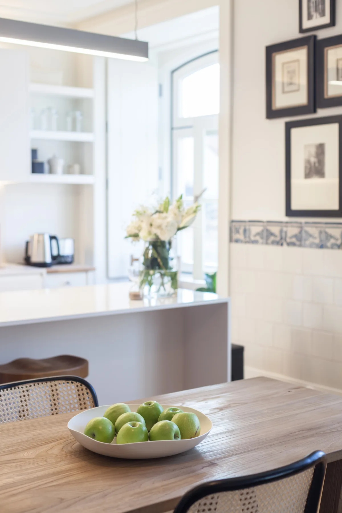 A bright dining area with a wooden table and a bowl of green fruit.