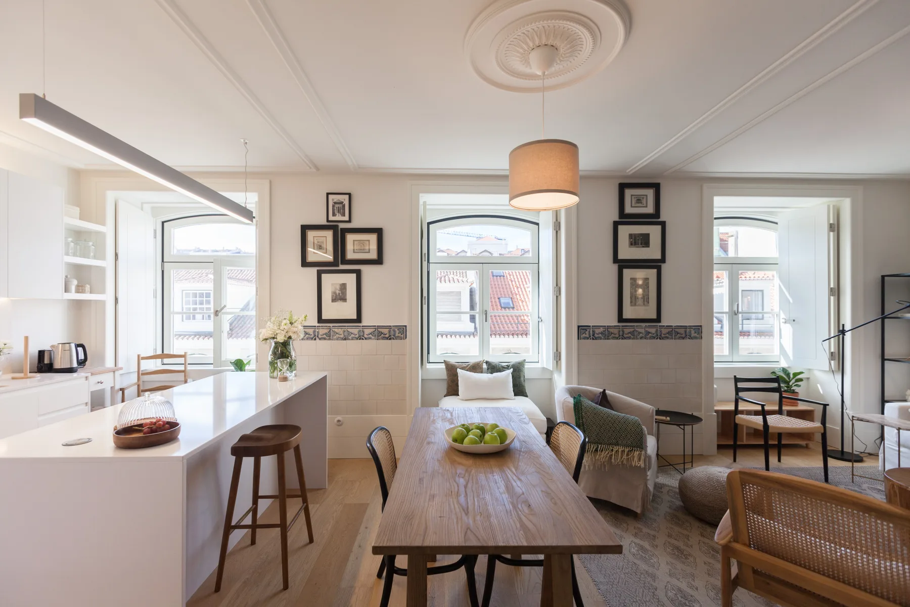 A bright dining and kitchen area with a long wooden table and large windows.