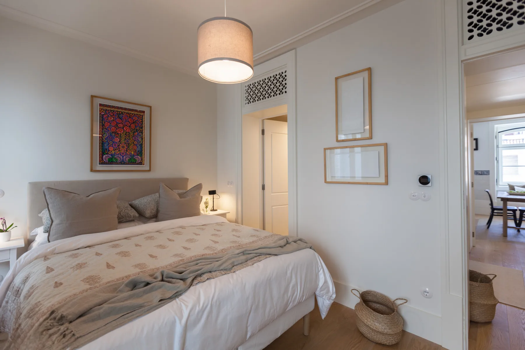 A bedroom with a bed, decorative pillows, and framed artwork on the wall.