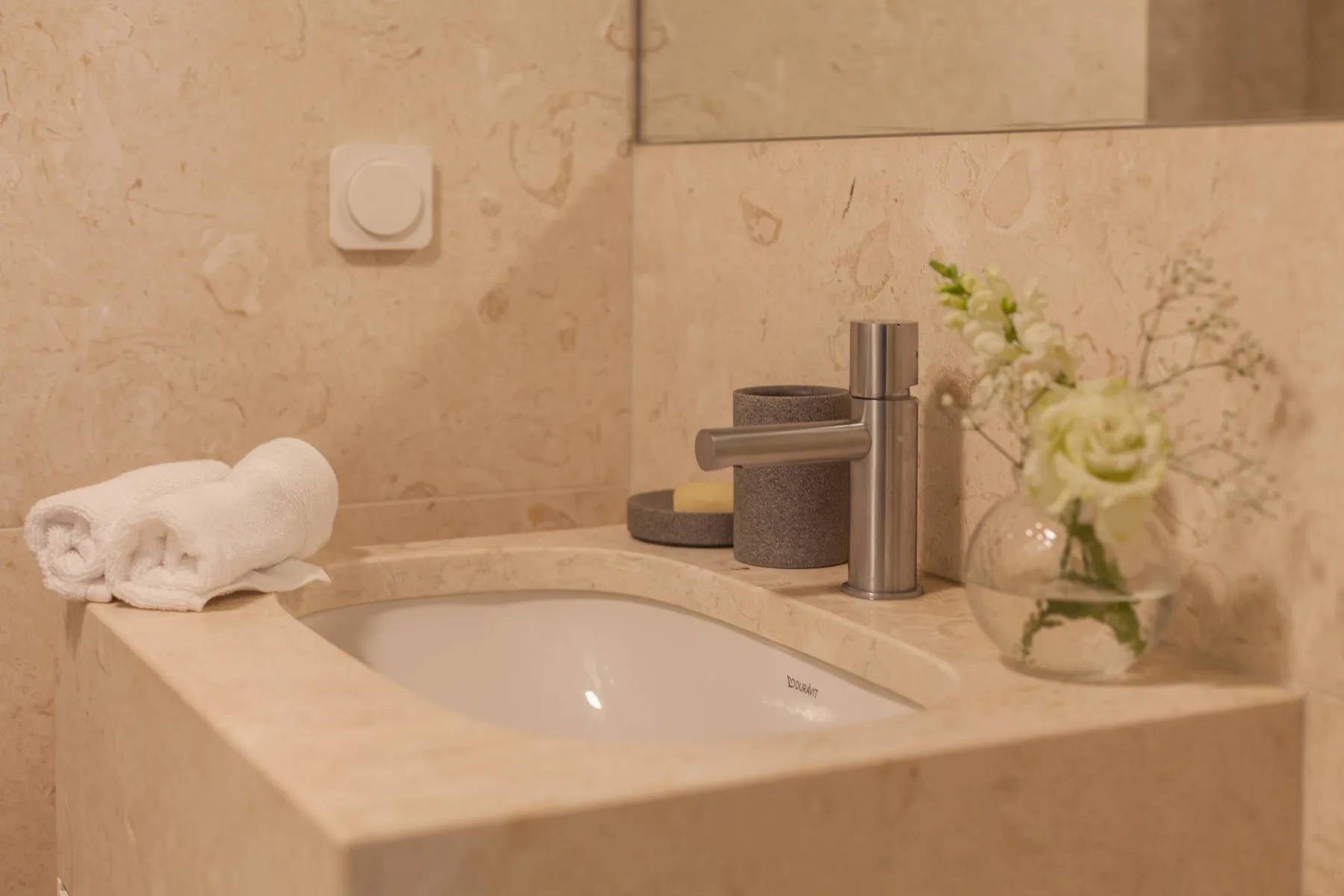 A bathroom vanity with a sink, folded towels, and a small flower arrangement.