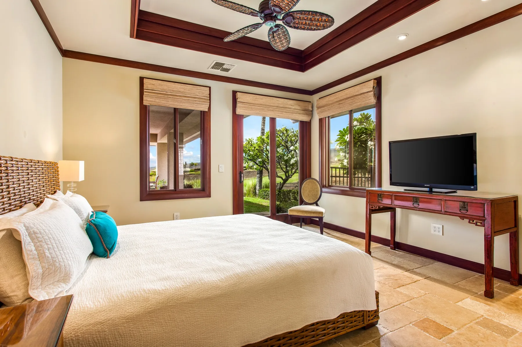 Dormitorio con cama, televisor y ventanas con vistas a vegetación frondosa.
