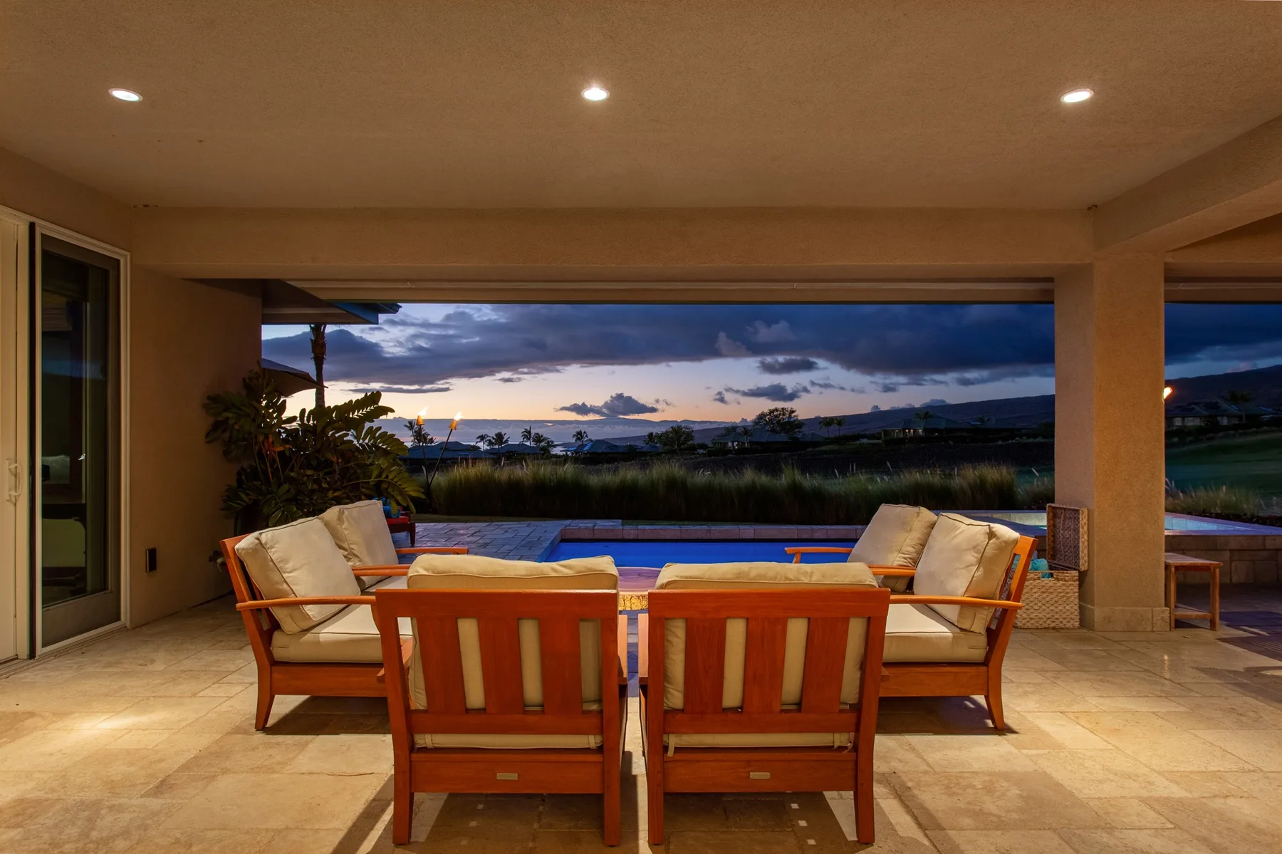 Asientos en un patio cubierto frente a una piscina y un cielo al atardecer.