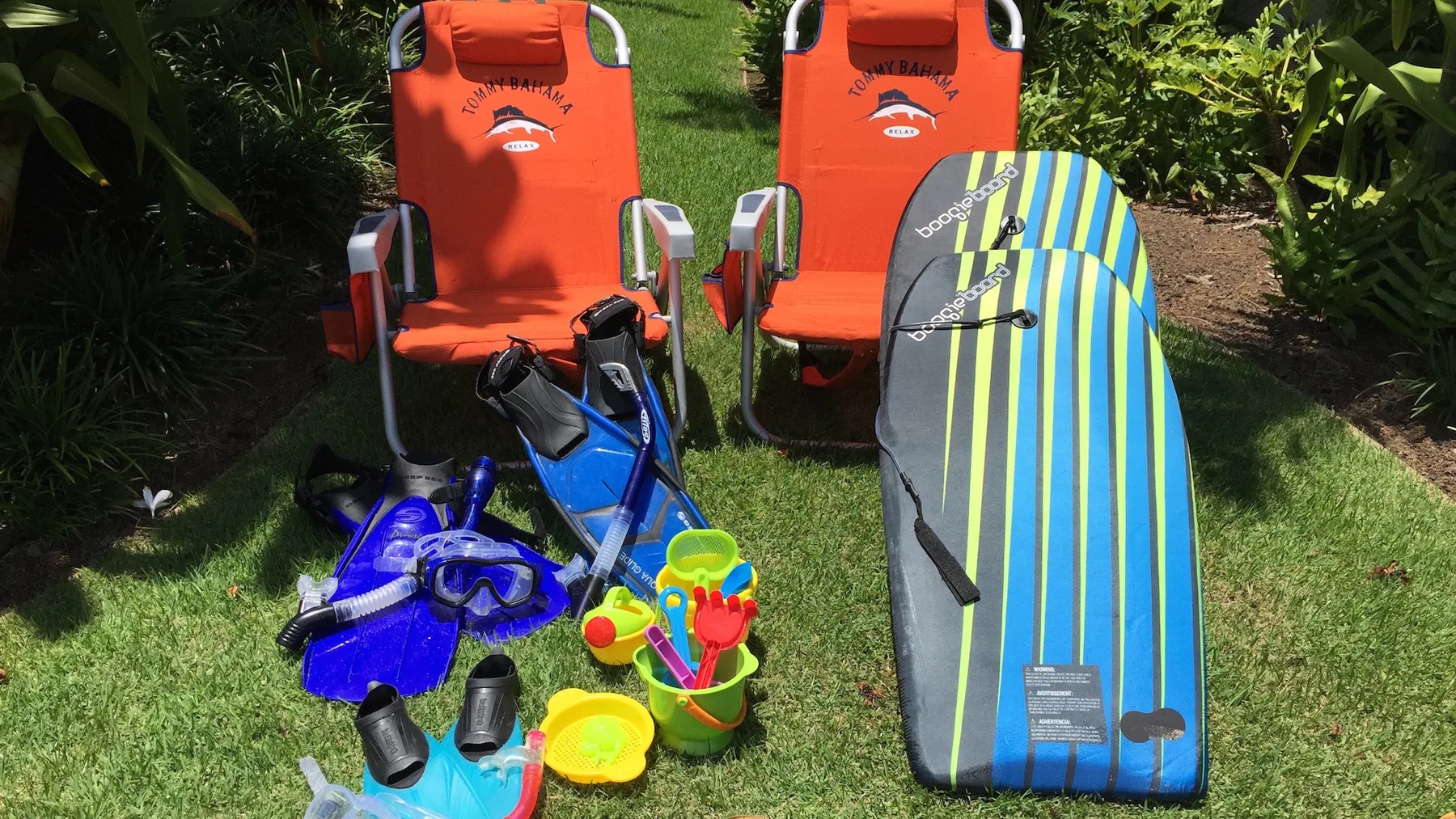 Equipo recreativo al aire libre, como sillas de playa, material de esnórquel y una tabla de bodyboard, sobre el césped.