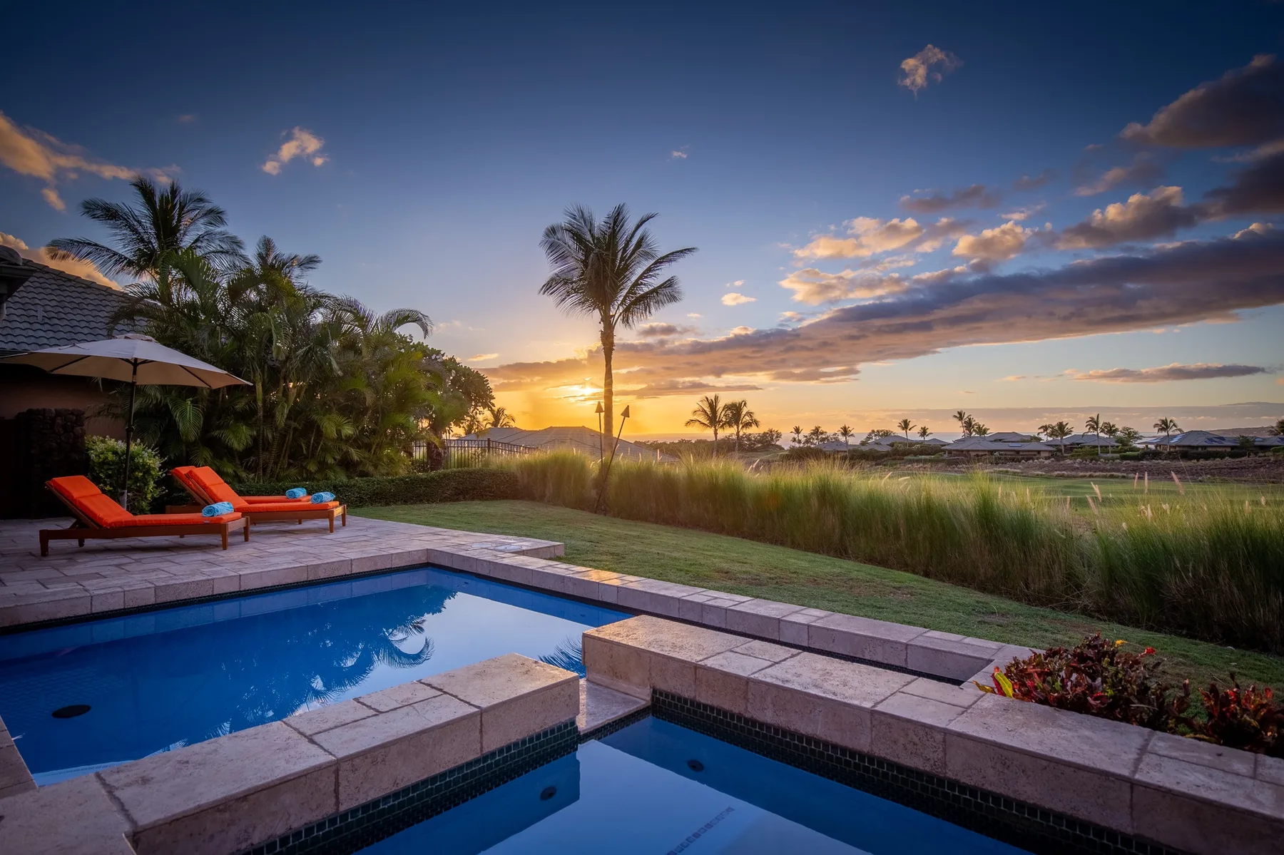 Una piscina junto a un jardín con césped ofrece vistas al océano al atardecer.