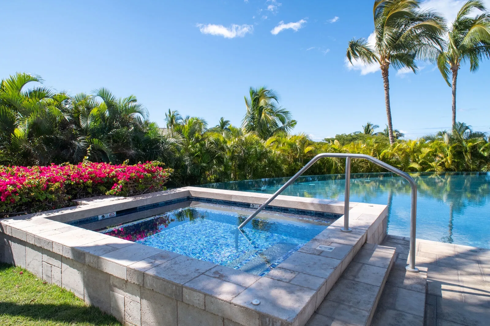 Una piscina pequeña de azulejos está junto a una piscina más grande, entre vegetación tropical.