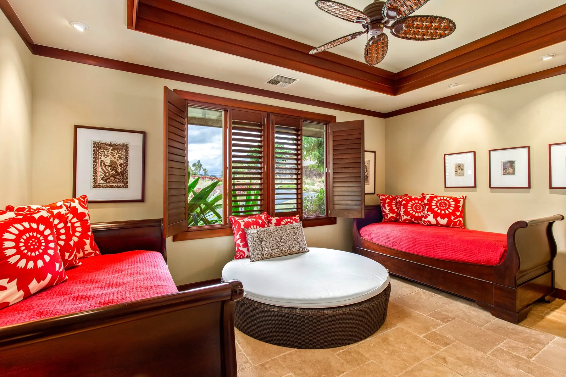 Una sala de estar con asientos acolchados rojos y una mesa redonda junto a ventanas con contraventanas.