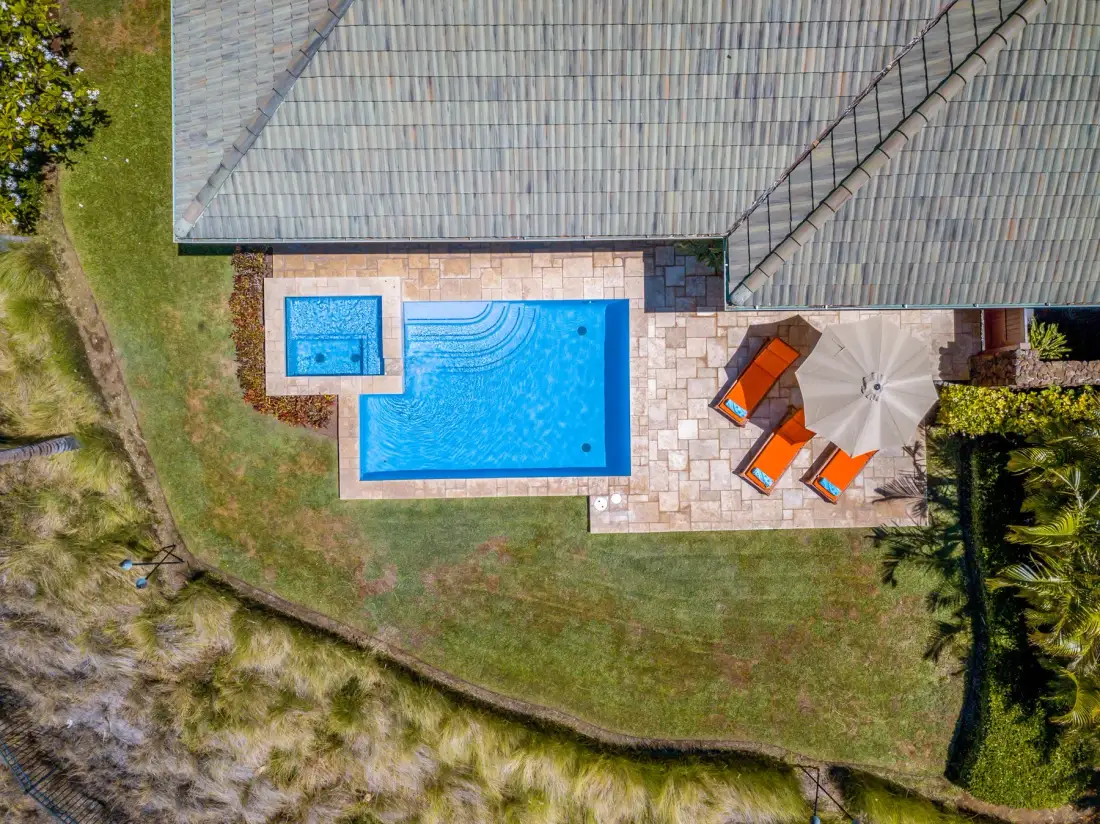 Vista aérea de una piscina y un patio pavimentado junto a una casa.
