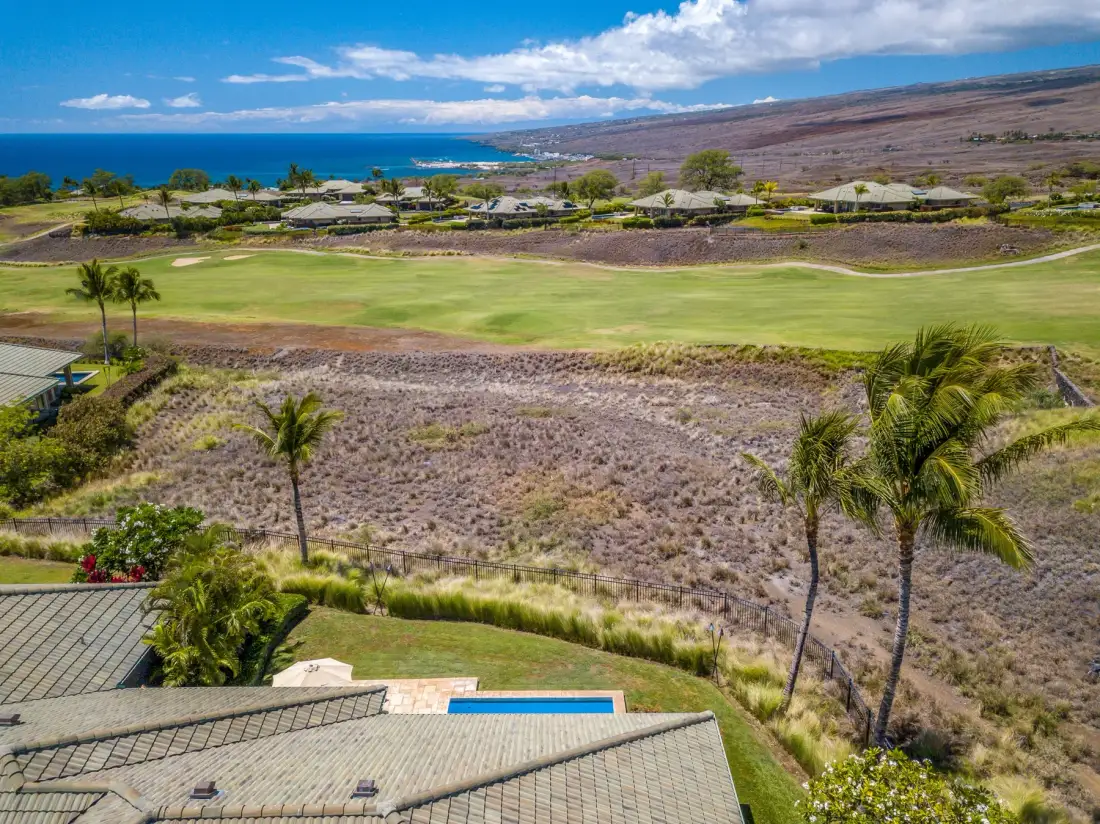 Paisaje costero con un campo verde, edificios bajos y el océano al fondo.