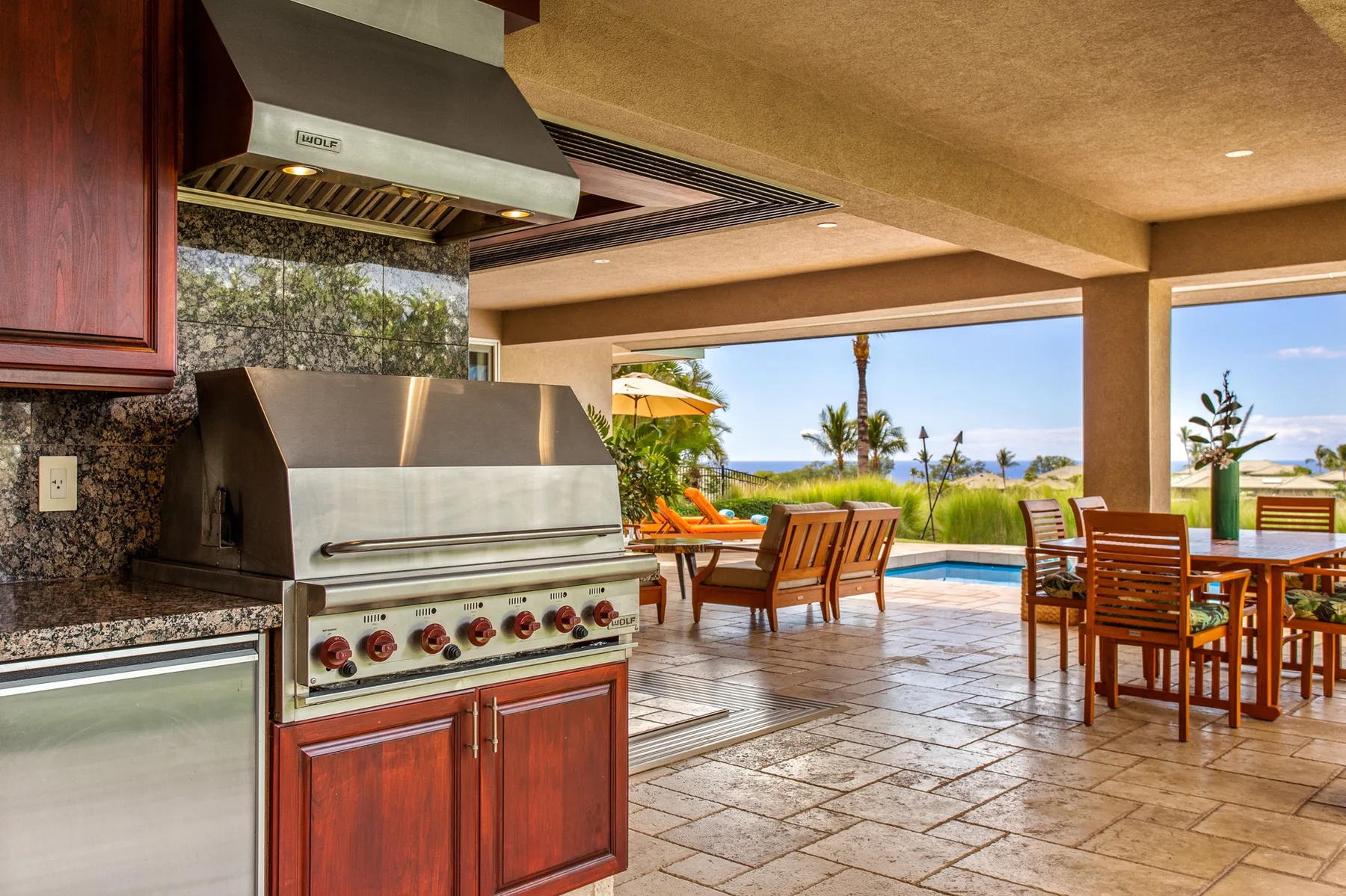Una cocina al aire libre y un comedor dan a una piscina y jardines.