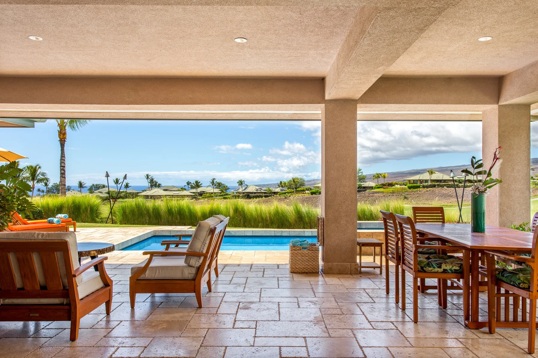 A covered patio with outdoor seating overlooks a swimming pool and landscaped grounds.