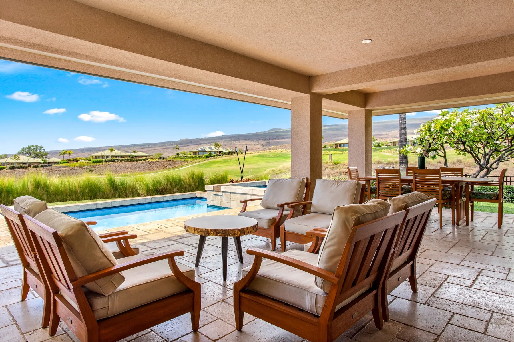 A covered patio with cushioned seating overlooks a swimming pool and open landscape.