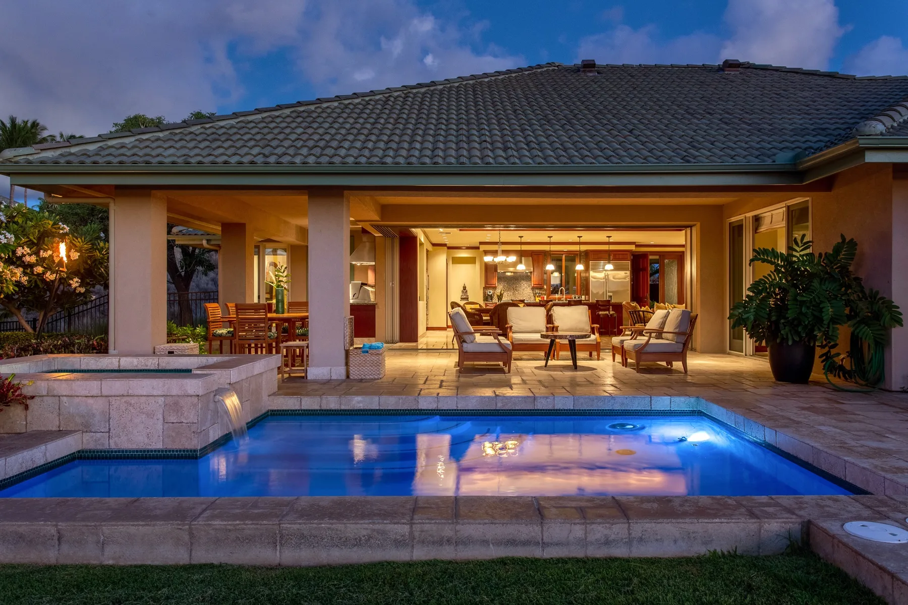 Una piscina está junto a un patio cubierto e iluminado, con asientos.