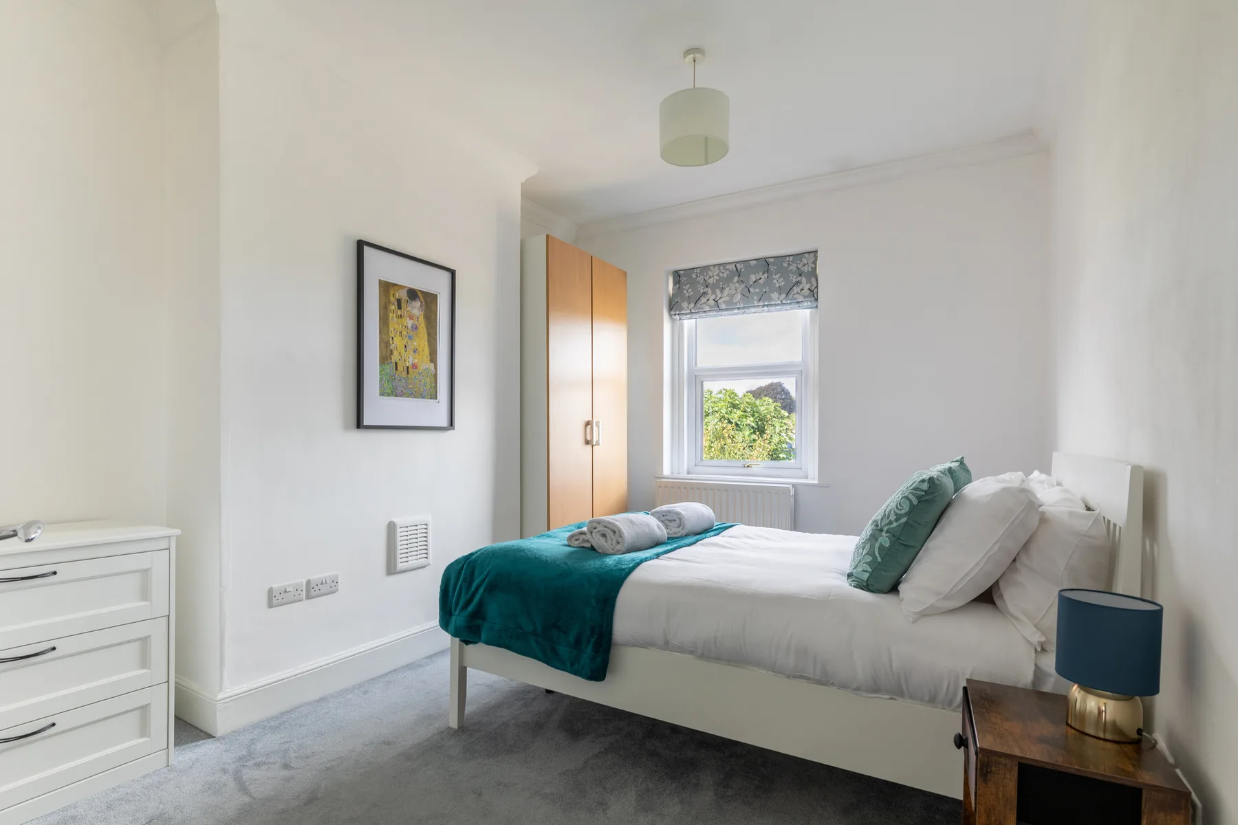 A bright bedroom with a bed dressed in white and teal bedding.