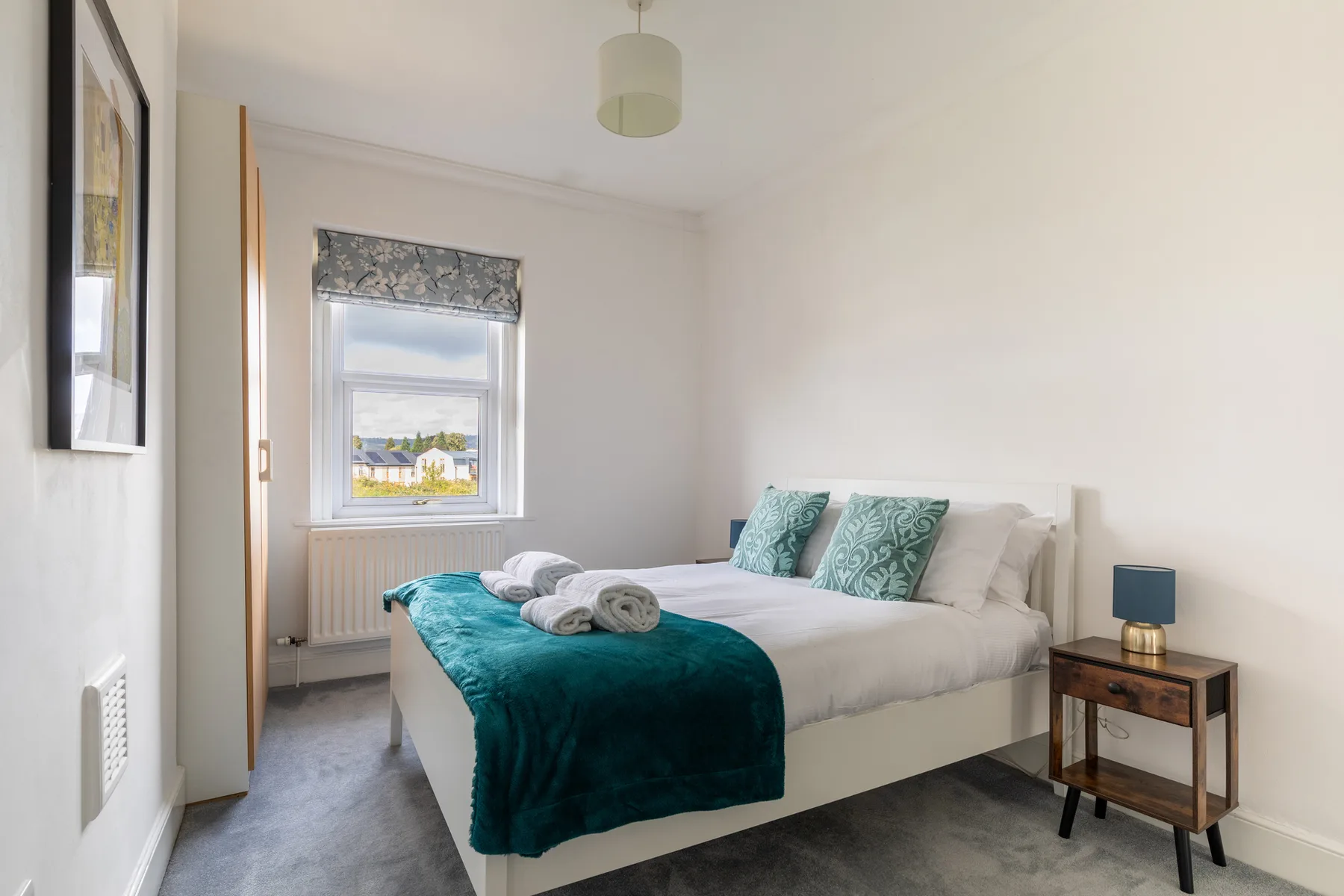 A bedroom with a neatly made bed and a teal blanket.