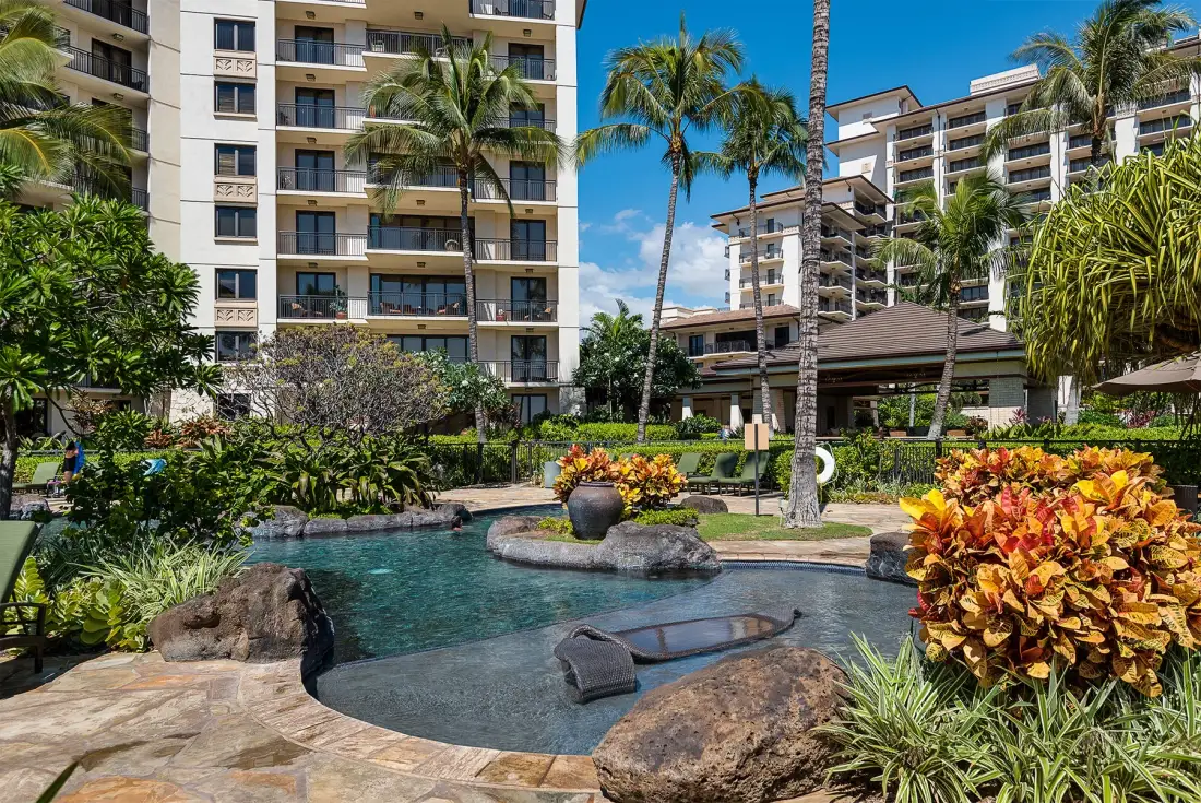 Un patio ajardinado con piscina está rodeado de edificios de apartamentos y palmeras.