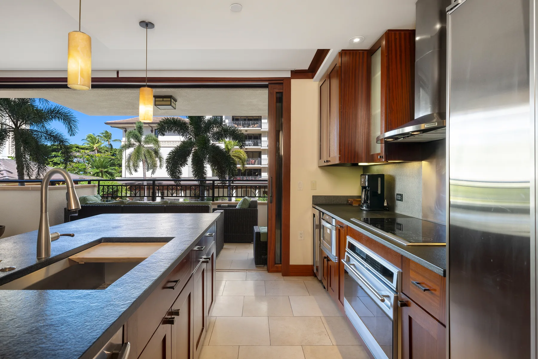 Una cocina moderna con una encimera larga y grandes ventanales con palmeras a la vista.