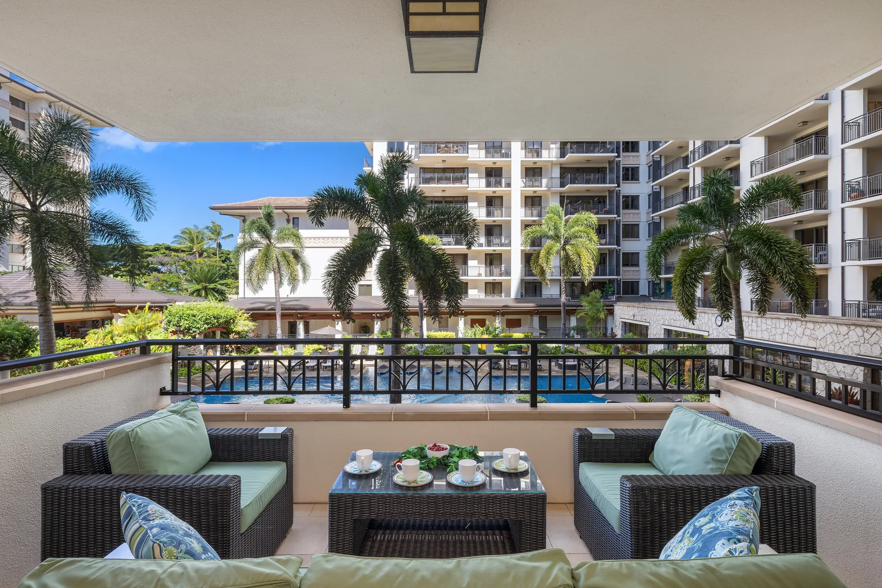 Una zona de estar exterior cubierta da a una piscina y palmeras.