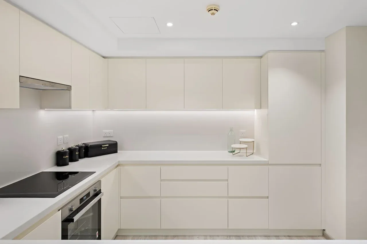 Una cocina moderna y luminosa con gabinetes blancos y una placa oscura.