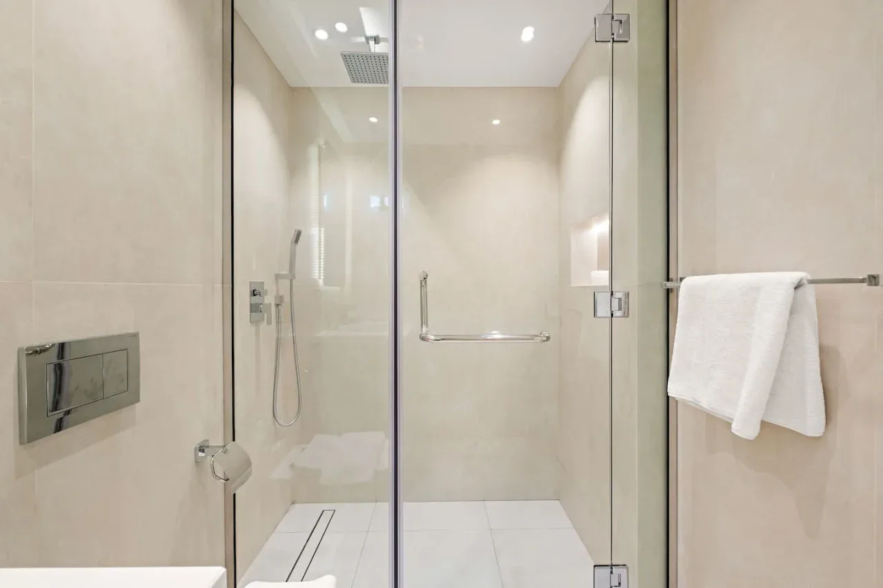 Un baño luminoso con una ducha de vidrio y una toalla colgada cerca.