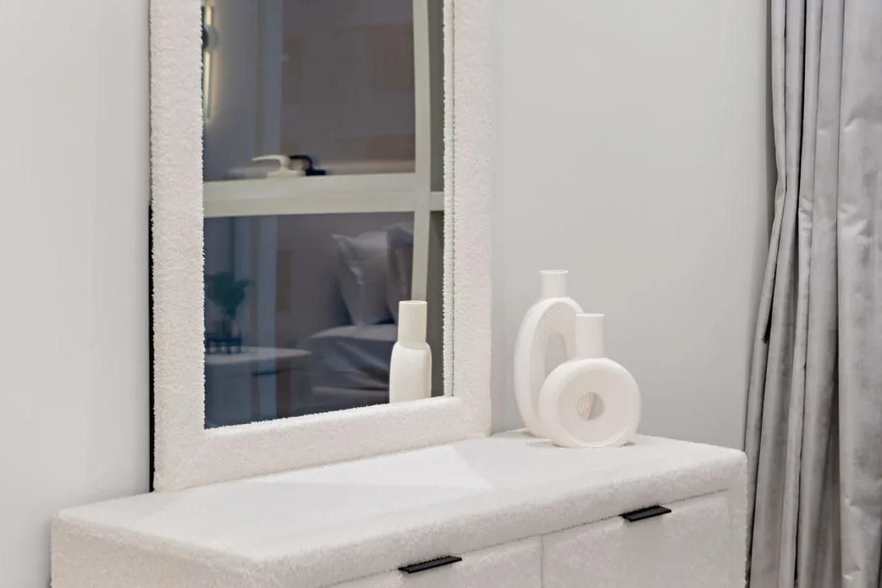 Una cómoda blanca de dormitorio con un espejo y objetos decorativos.