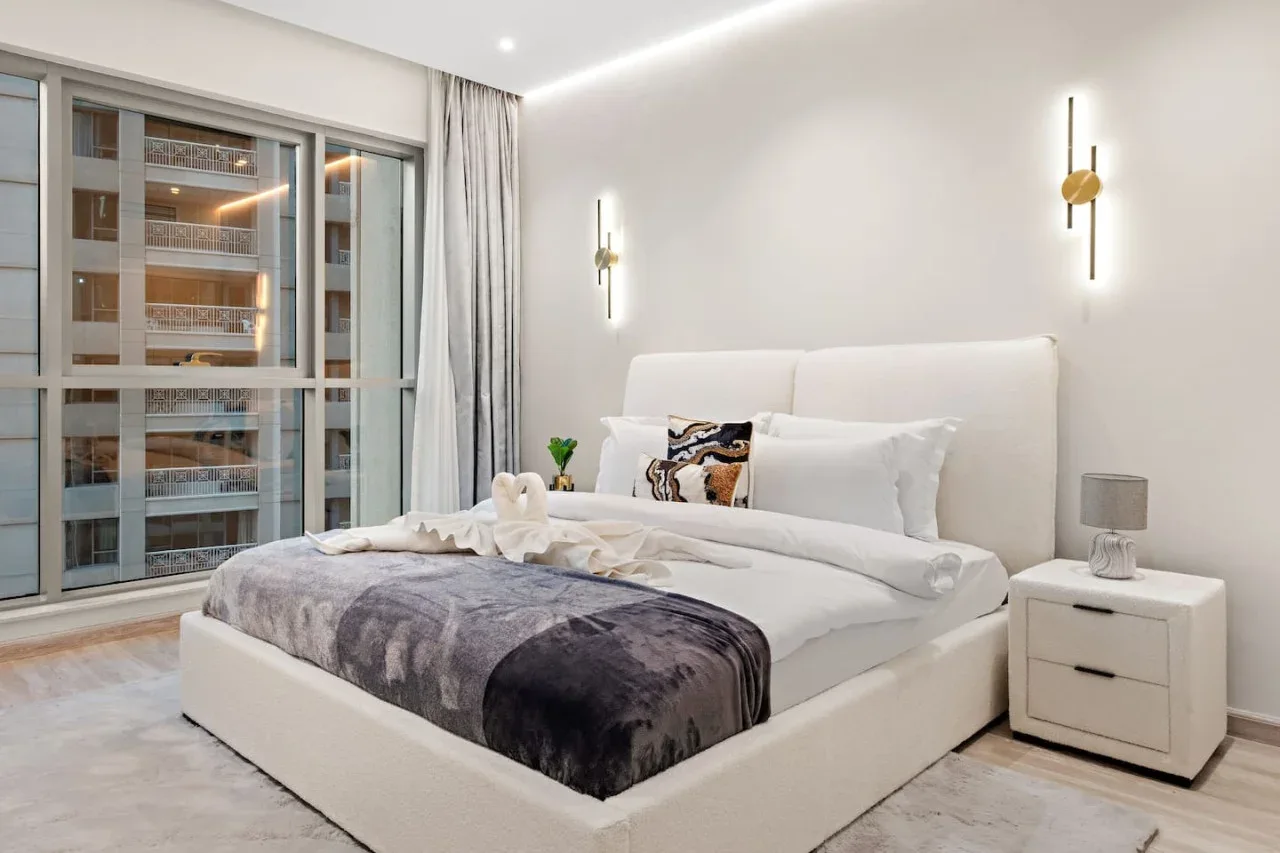 Un dormitorio luminoso con una cama arreglada junto a una ventana grande.