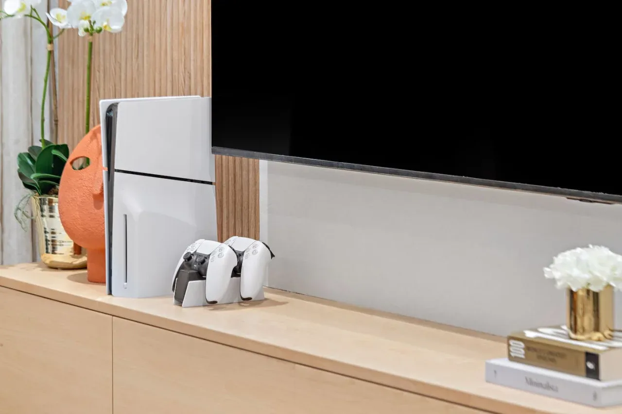 Un mueble de sala sostiene un televisor, una consola de videojuegos y controles.