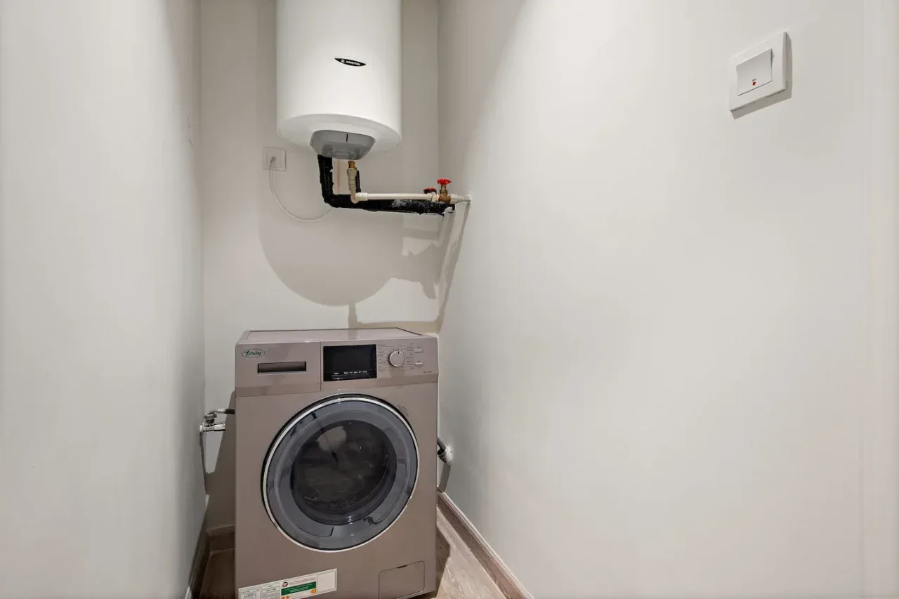 Zona de lavandería con lavadora de carga frontal y calentador de agua en la pared.