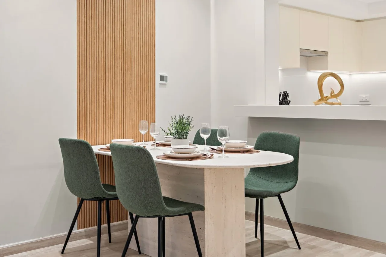 Comedor con la mesa puesta y asientos verdes junto a la cocina.