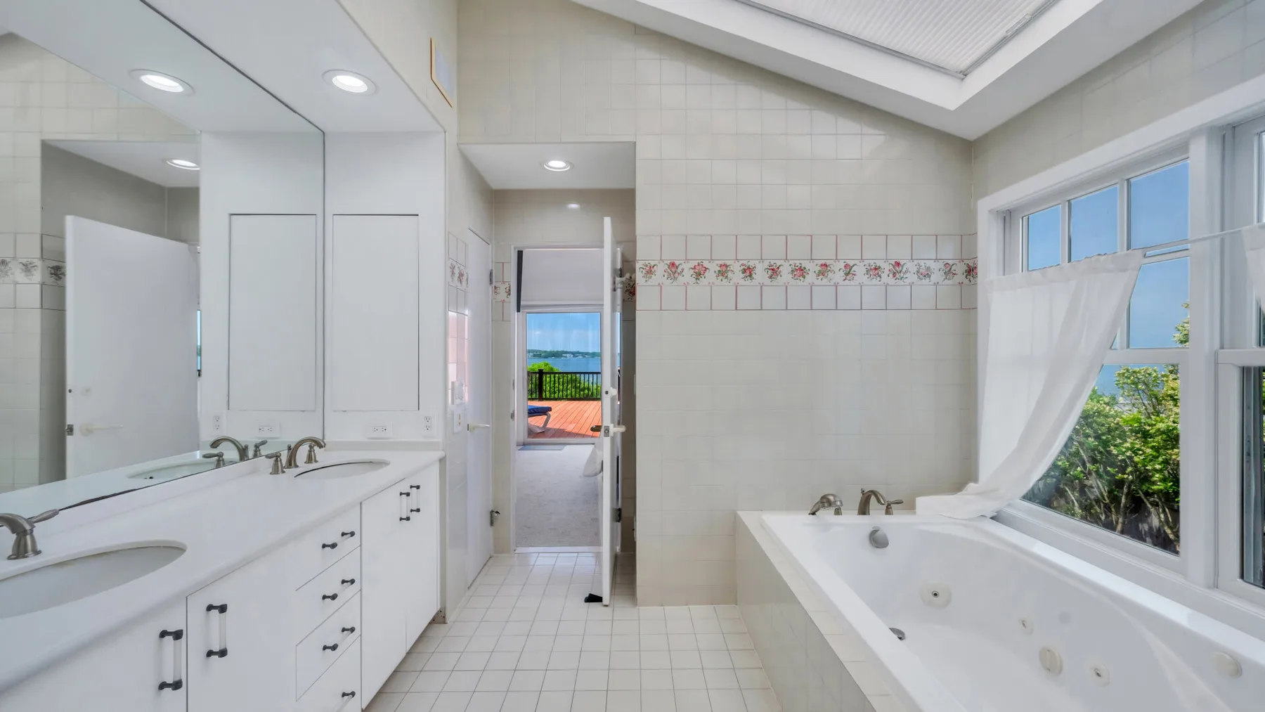 Un baño luminoso con un largo tocador y una bañera grande junto a la ventana.