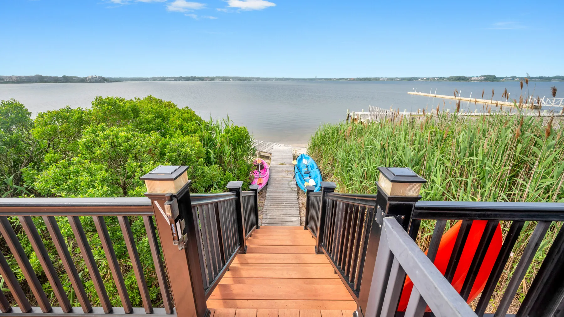 A wooden deck walkway leads through shoreline vegetation to a calm body of water.
