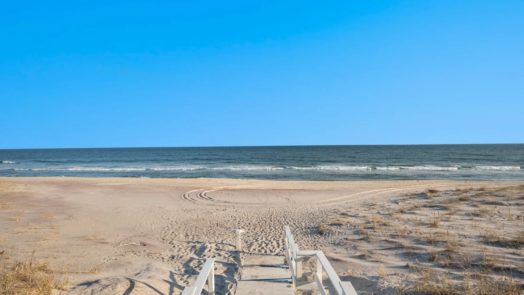 Una playa de arena con un sendero de madera que lleva al océano.