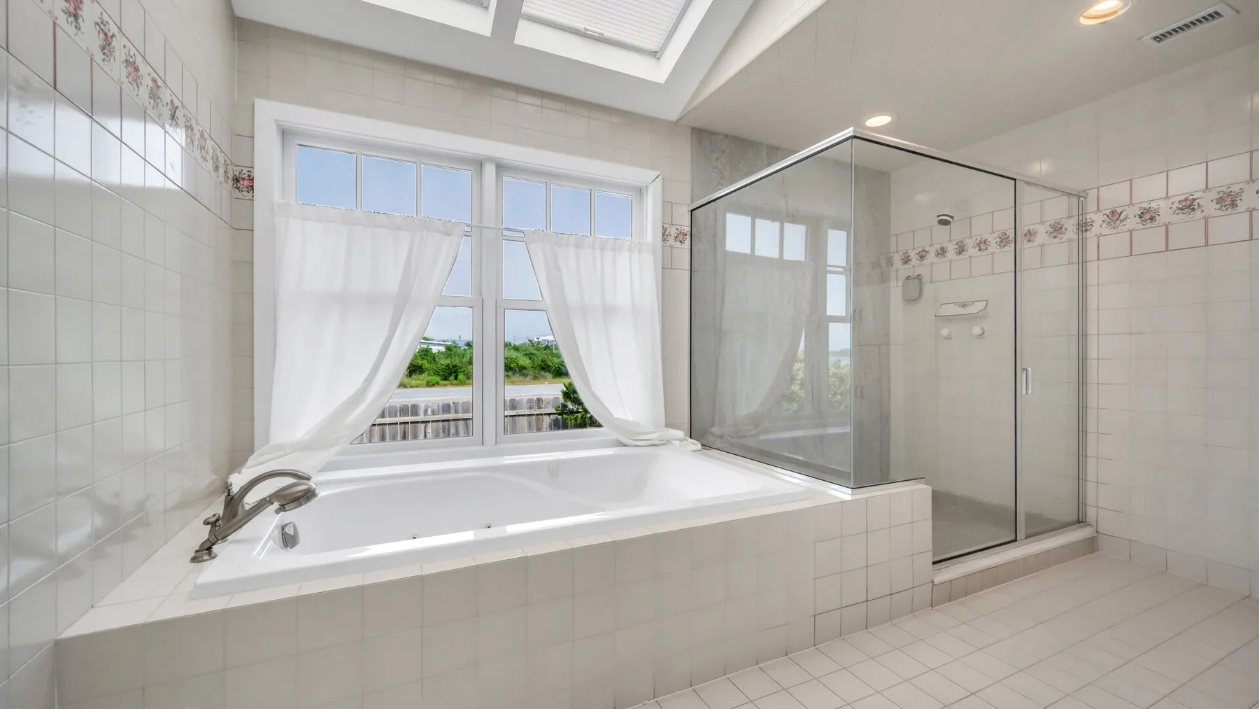 Un baño luminoso con azulejos, bañera, ducha de vidrio y una ventana grande.