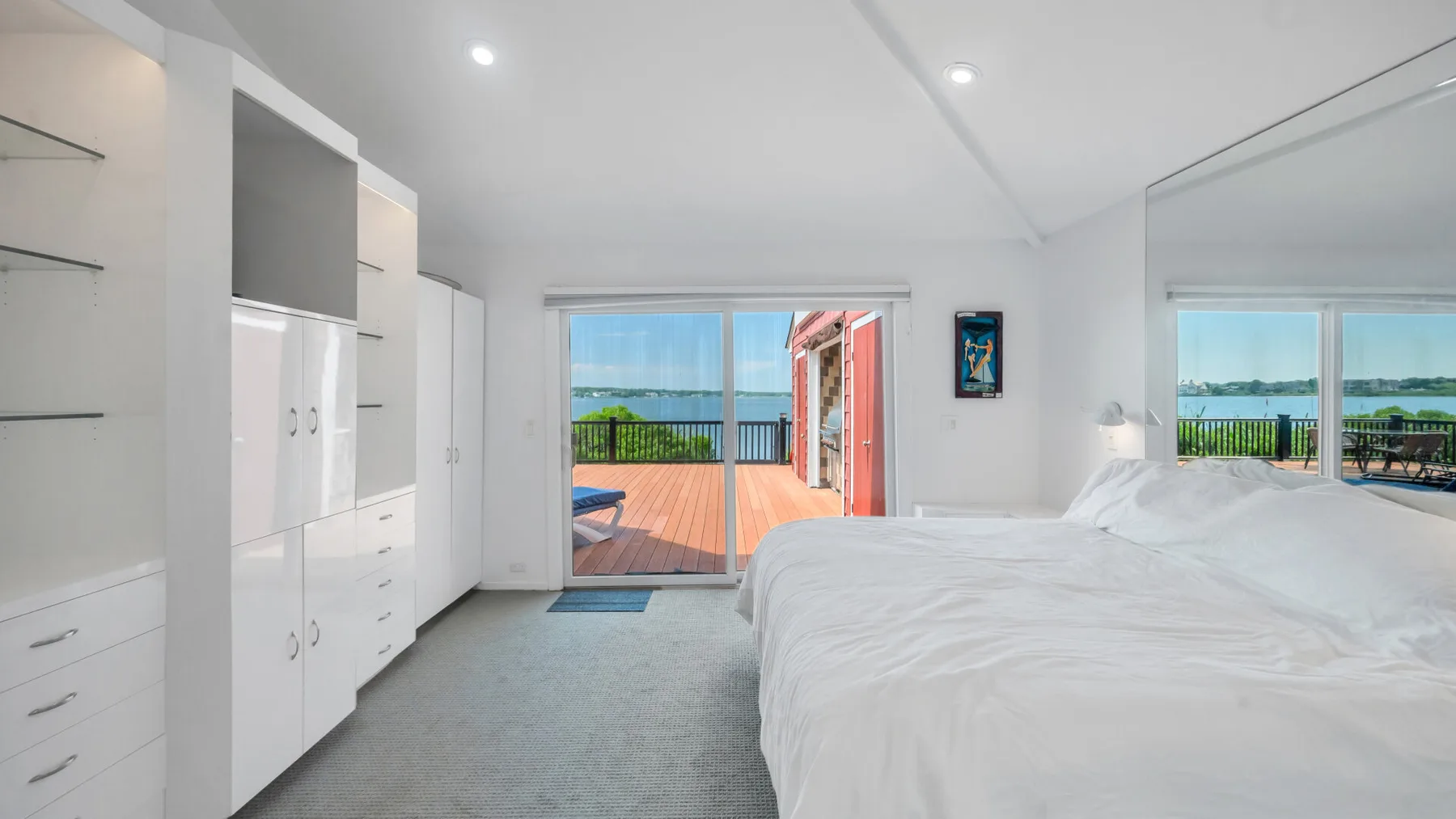Un dormitorio luminoso con una cama junto a puertas de vidrio que dan a una terraza de madera.