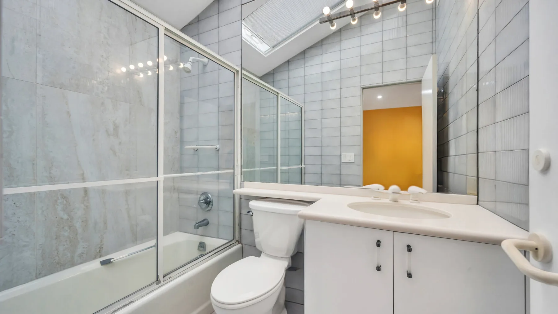 Un baño con azulejos, ducha de vidrio, inodoro y lavabo con mueble.