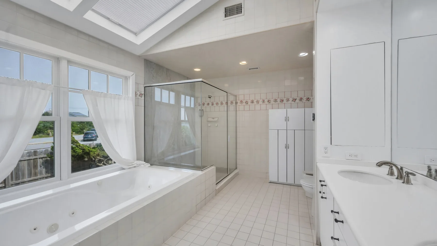 Un baño luminoso con una bañera junto a grandes ventanas y una ducha de vidrio.