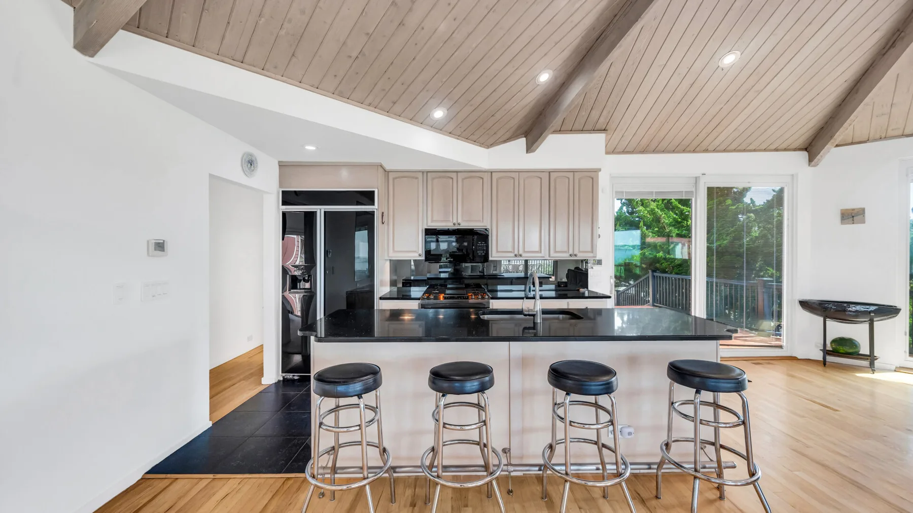 Una cocina luminosa con una isla central y taburetes bajo un techo abovedado de madera.