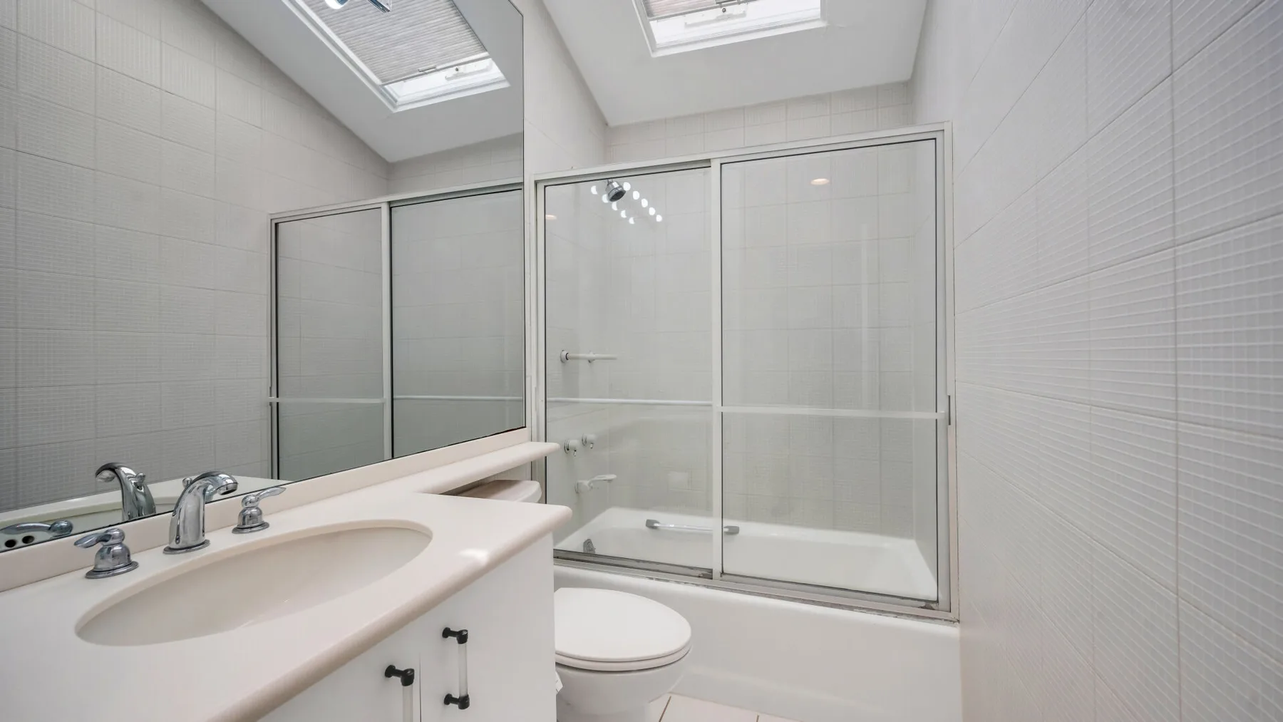Un baño luminoso con azulejos, un lavabo largo y una ducha de vidrio.