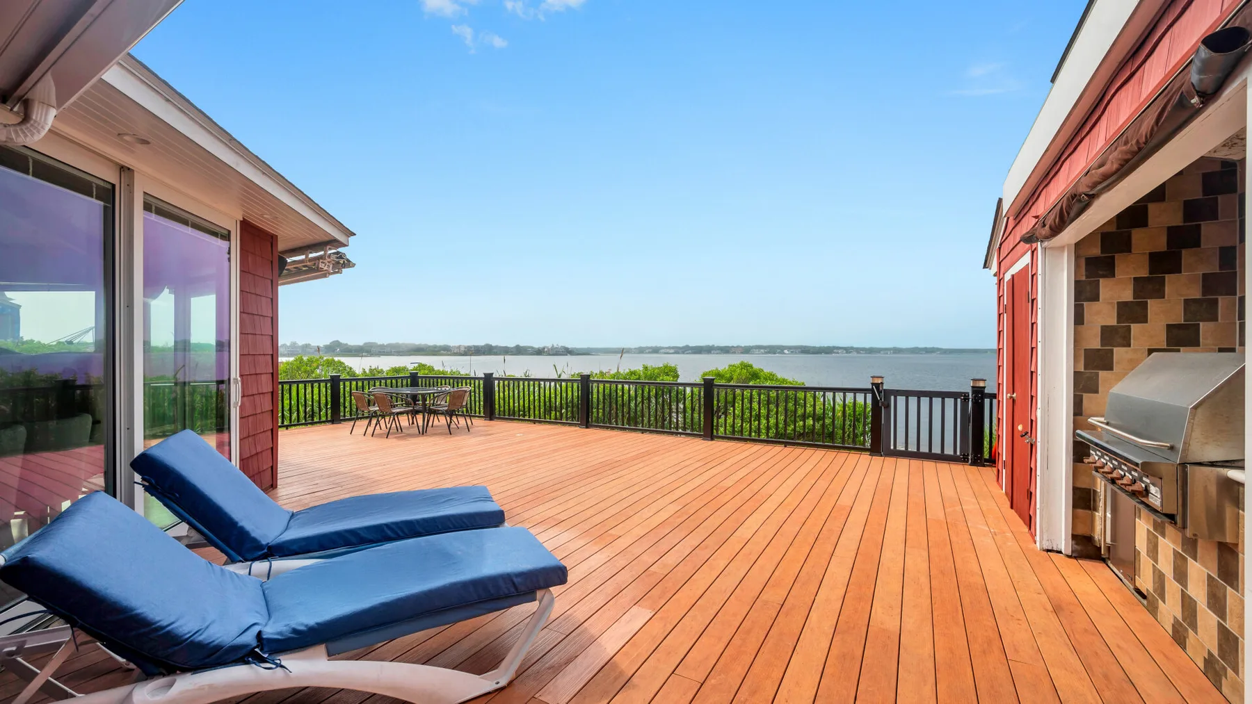 A spacious wooden deck overlooks the water, with lounge seating and a built-in grill.